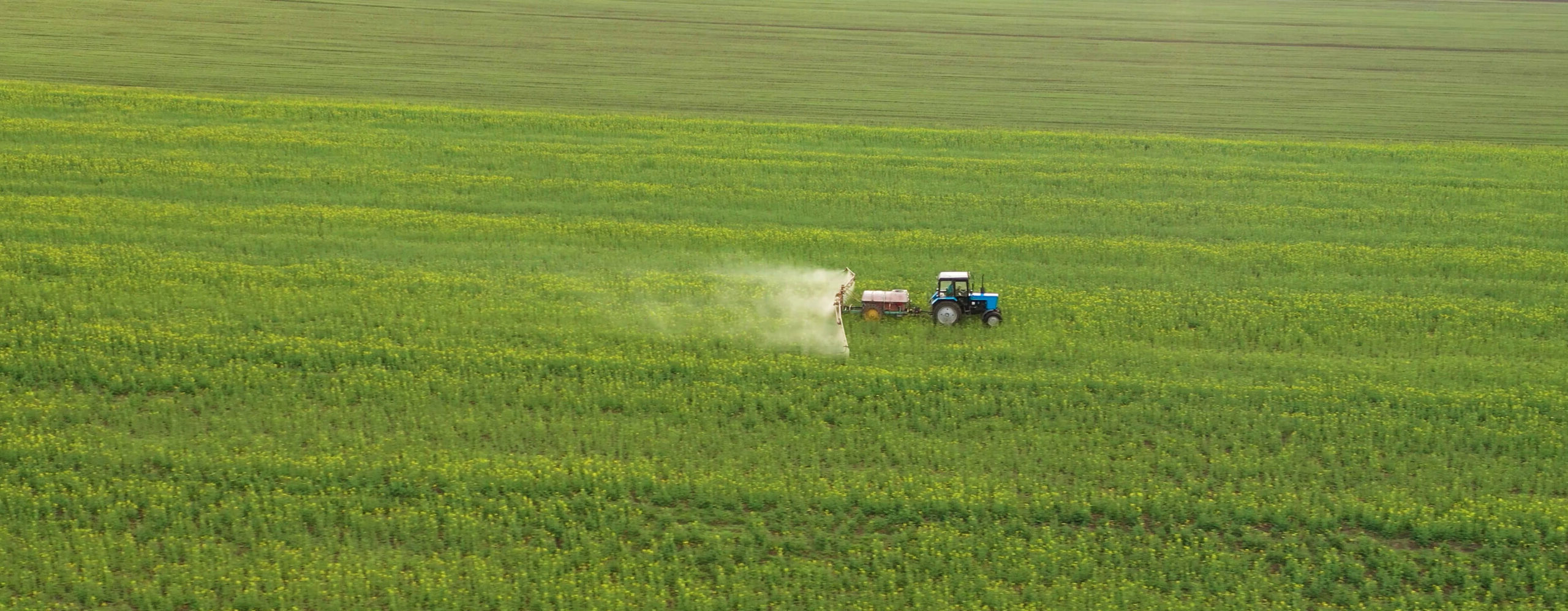 Aerial view of a tractor spraying fertilizer on a green field.